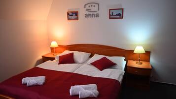 Una cama bien hecha con ropa de cama roja y blanca, dos lámparas de noche y una pared con cuadros enmarcados y un logotipo.