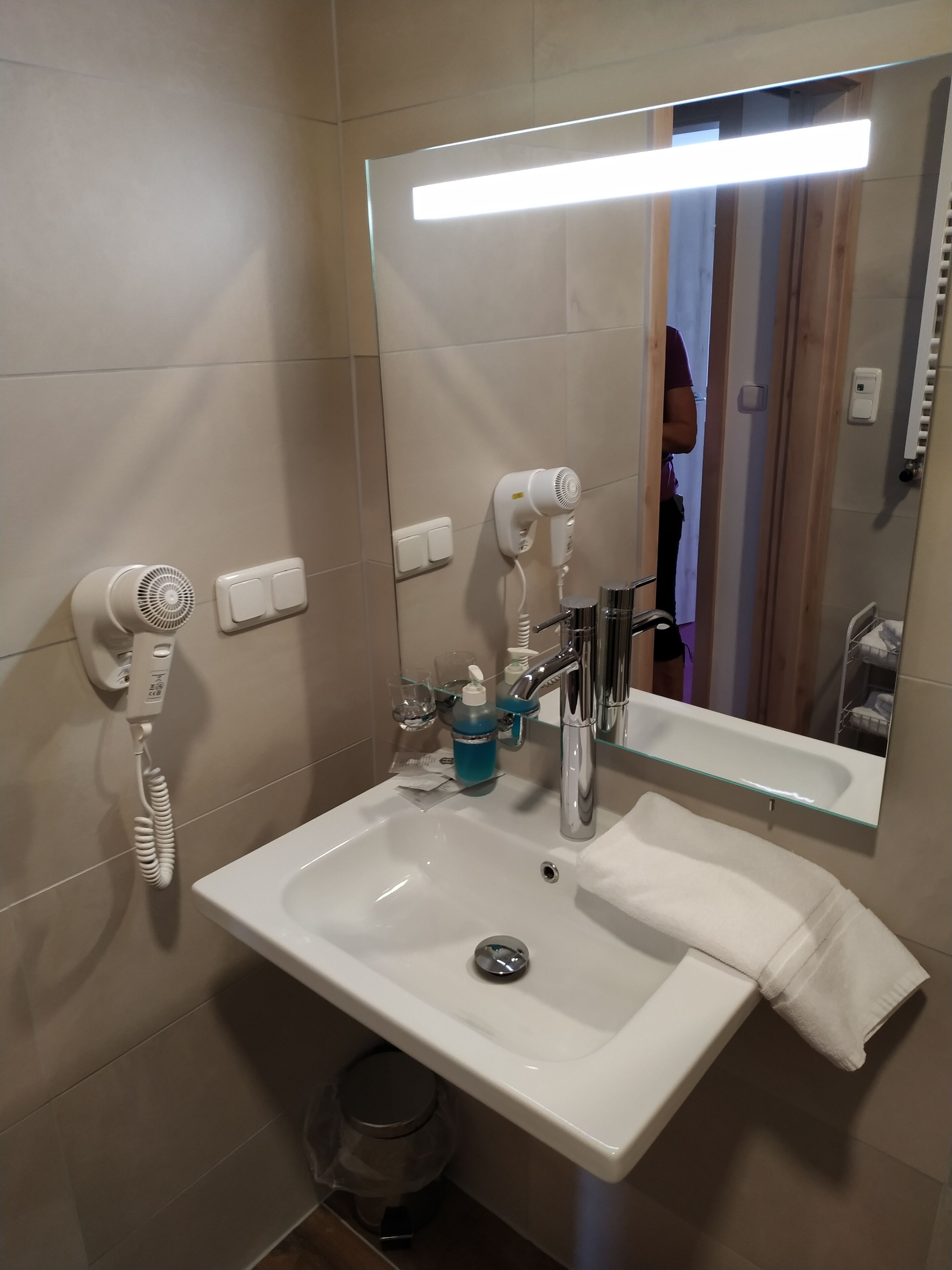 Un baño con lavamanos blanco, espejo, secador de pelo y toallero.