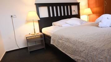 Een hotelkamer met een bed, twee bedlampjes, een nachtkastje en een stopcontact.