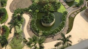 A multi-story residential building with a landscaped courtyard featuring palm trees, circular gardens, and a central water feature.
