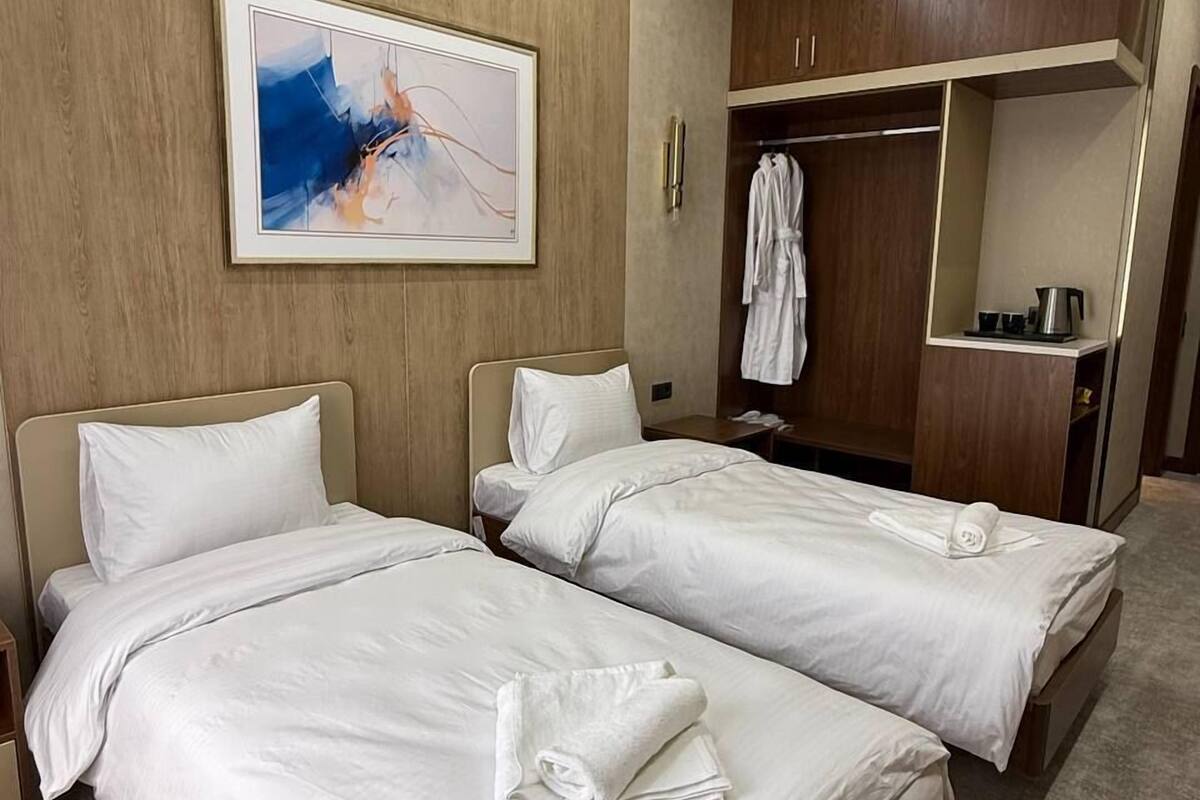 Habitación de hotel con dos camas, un armario de madera, un cuadro en la pared y una mesita con una tetera.
