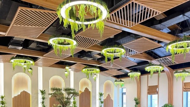 Un'ampia sala da pranzo con diversi tavoli e sedie, caratterizzata da un design moderno con dettagli in legno e piante pensili.