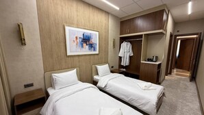 Camera d'albergo con due letti, un armadio, un quadro e un appendiabiti.