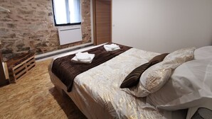 A bedroom with a stone wall, a wooden bed frame, a window with curtains, and a wooden wardrobe. - Gîte Corrézien 3 pers. Heated swimming pool (Chamboulive)
