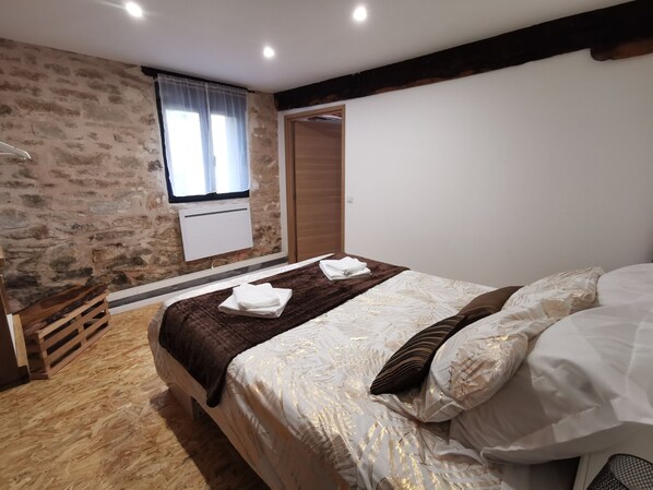 A bedroom with a stone wall, a wooden bed frame, a window with curtains, and a wooden wardrobe. - Gîte Corrézien 3 pers. Heated swimming pool (Chamboulive)