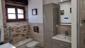 A compact bathroom with a stone wall, a toilet, a sink, and a mirror. - Gîte Corrézien 3 pers. Heated swimming pool (Chamboulive)
