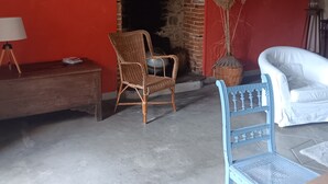 Un intérieur rustique avec une cheminée en briques, un fauteuil en osier, un canapé blanc et une petite table avec une lampe.
