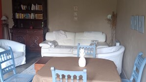 Un salon chaleureux avec un canapé blanc, des fauteuils bleus, une table basse en bois et une bibliothèque remplie de livres.
