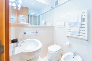 Moderni kylpyhuone, jossa on wc, bidee, pesuallas ja pyyhekoukku.