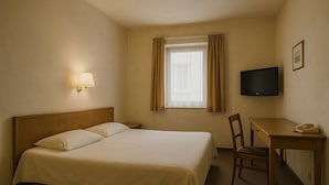 A hotel room with a bed, a desk, a chair, a television, and a window with curtains. - Le Patron Hotel (Lahr)