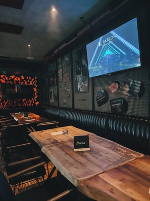 A restaurant interior with a long wooden table, a booth seating area, and a screen displaying 'The Patron Party Mode'. - Le Patron Hotel (Lahr)