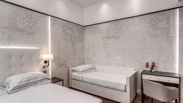A modern hotel room with a large bed, a smaller bed, a desk with a chair, and a nightstand with a lamp.