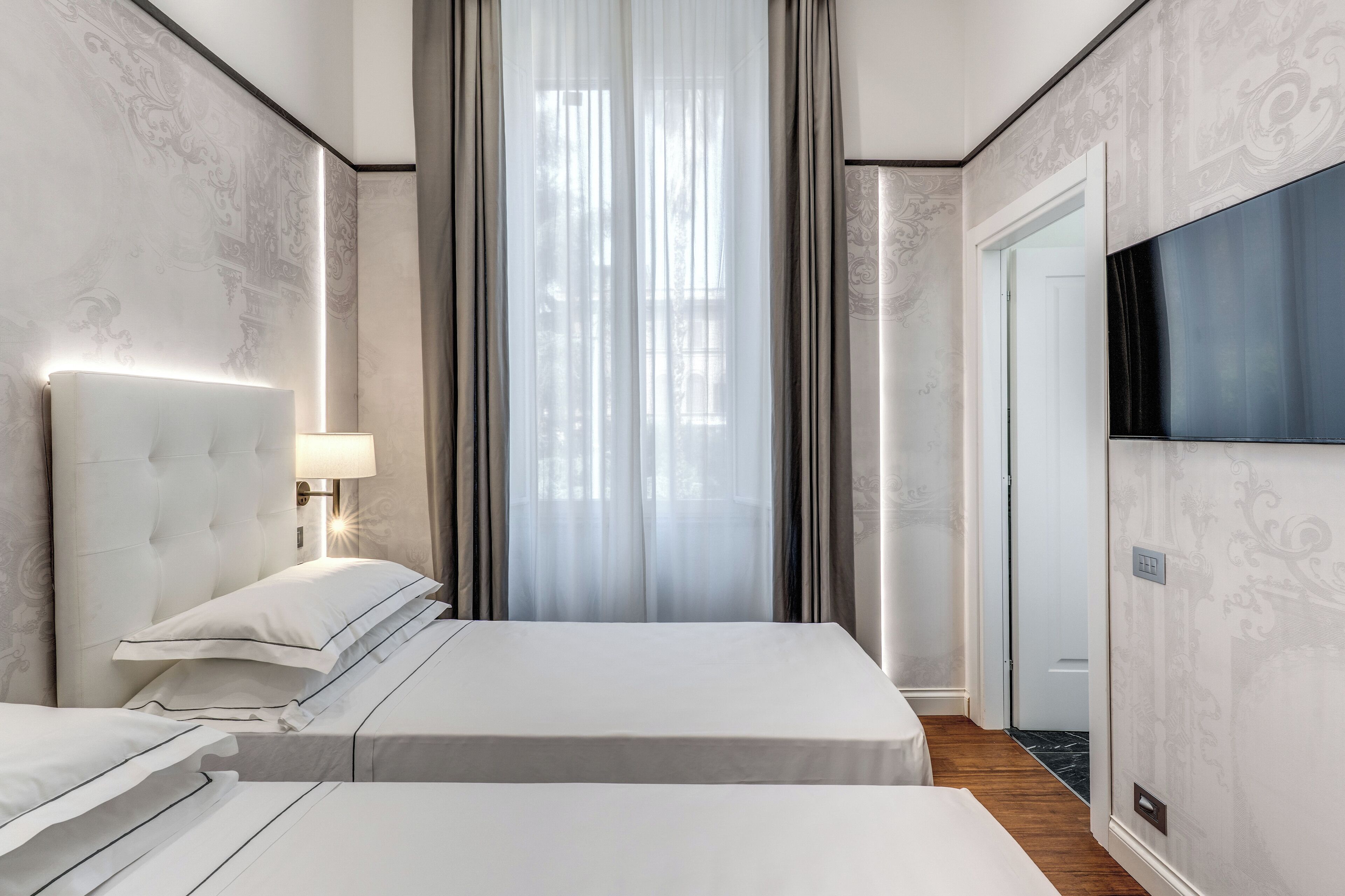 A hotel room with a bed, a bedside lamp, a TV, and a window with curtains.