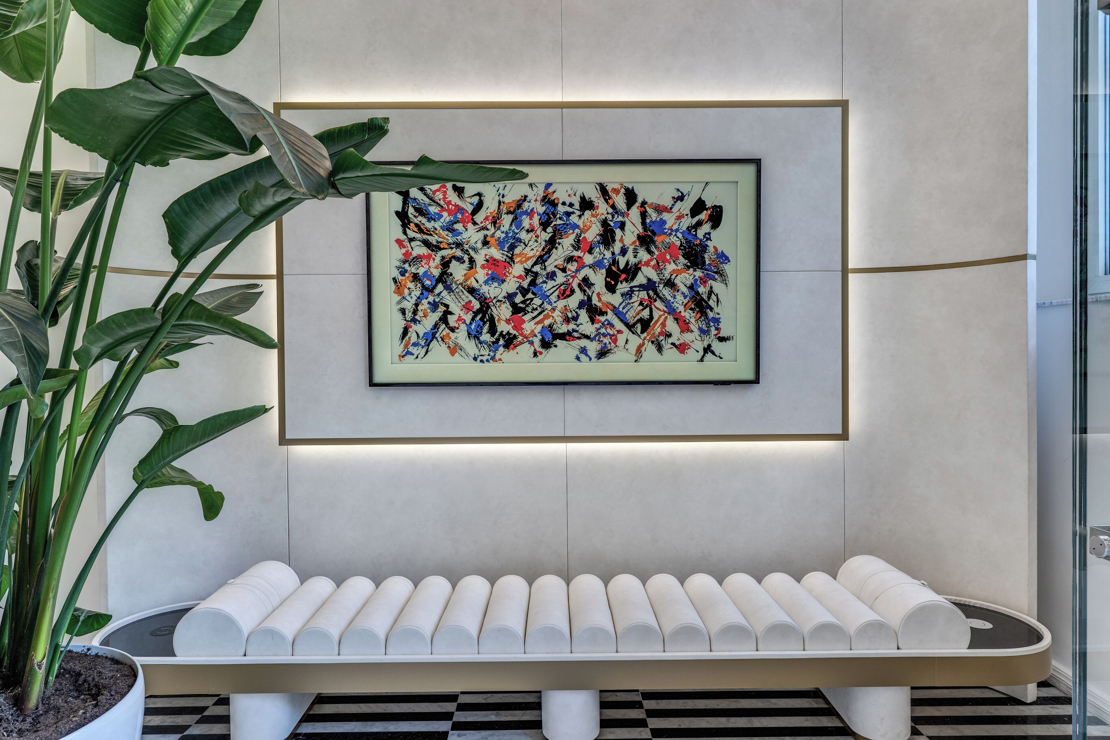 A modern interior with a bench, a framed abstract painting, and a potted plant.