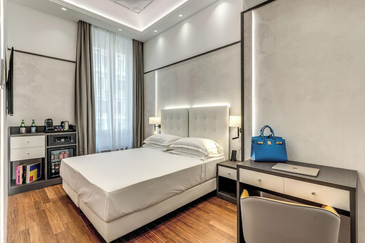 A modern hotel room with a large bed, a desk, a chair, and a minibar.