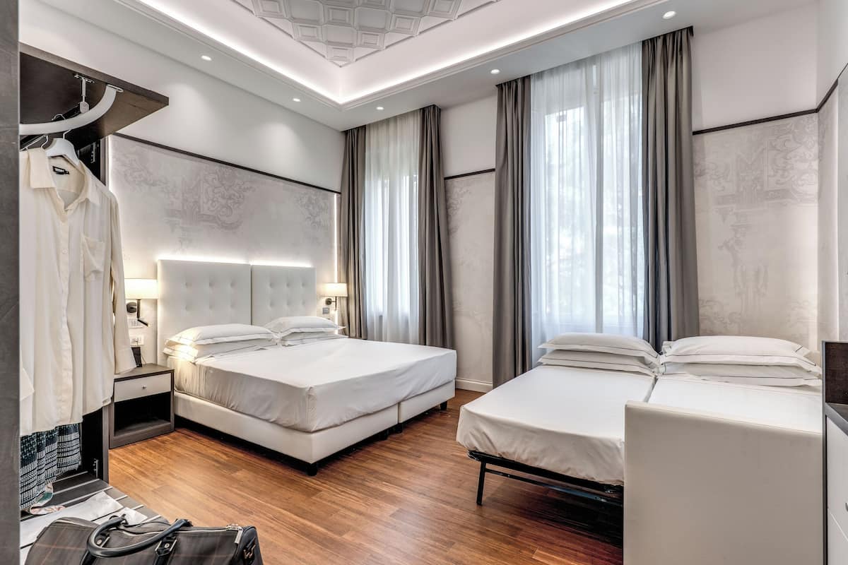 A modern hotel room with two beds, a wardrobe, a desk, and a large window with curtains.