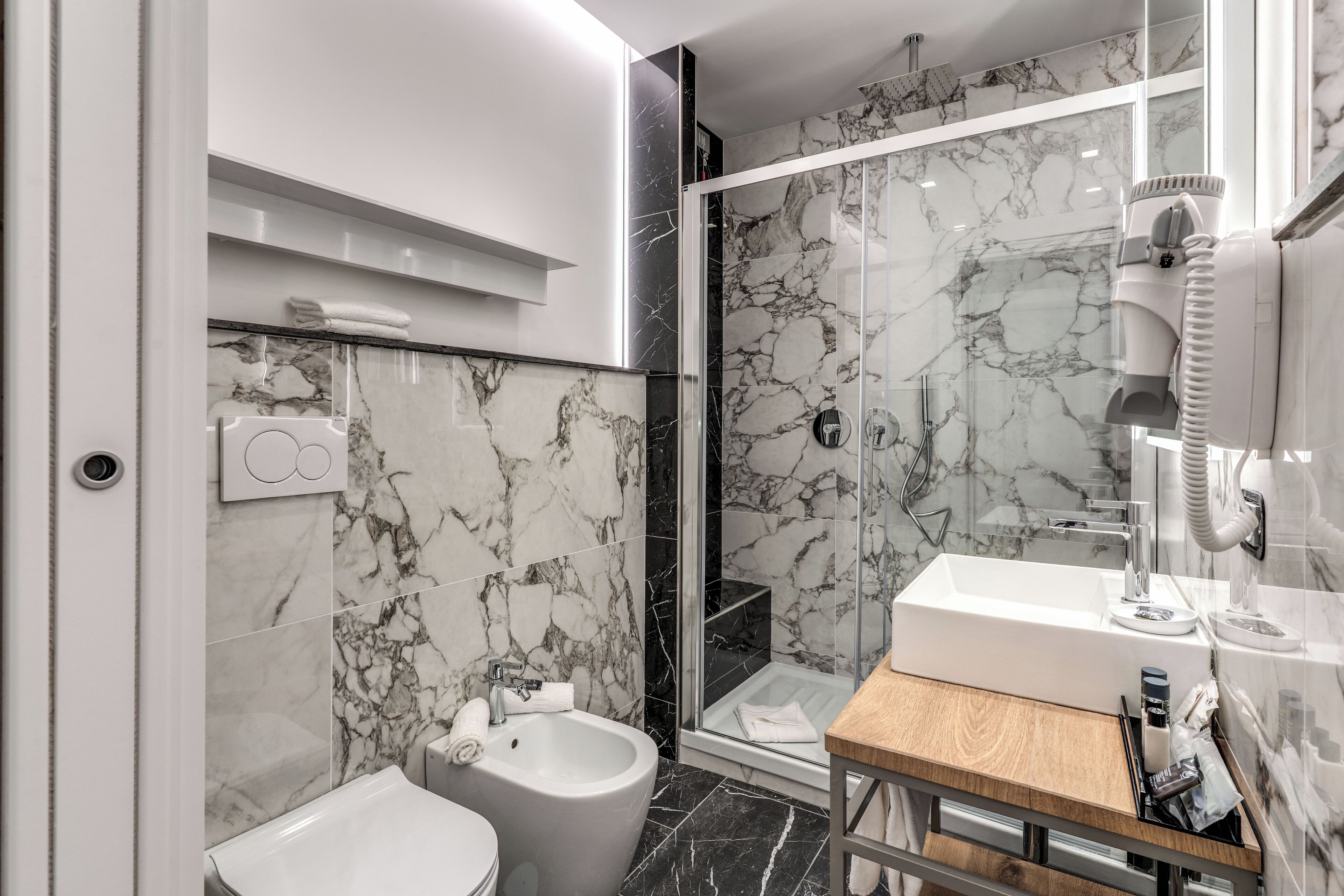 A modern bathroom with a bidet, a glass shower enclosure, and a wooden vanity with a sink.