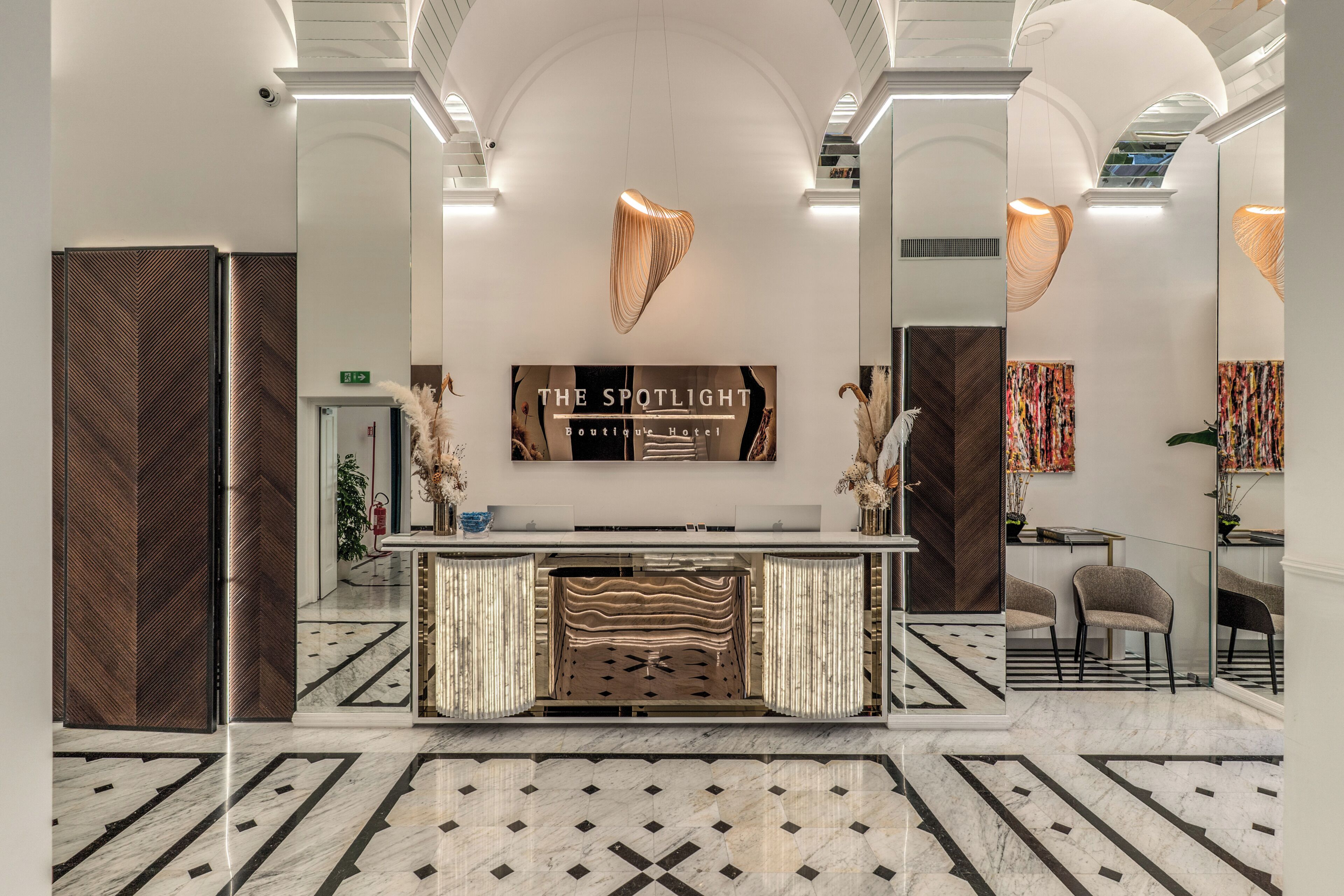 A hotel reception area with a modern design, featuring a marble floor, a reception desk, and a sign that reads 'THE SPOTLIGHT Boutique Hotel'.
