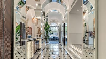 Un hall spacieux et bien éclairé, doté d’un sol en marbre, de grandes fenêtres et d’un escalier central menant à l’étage supérieur.