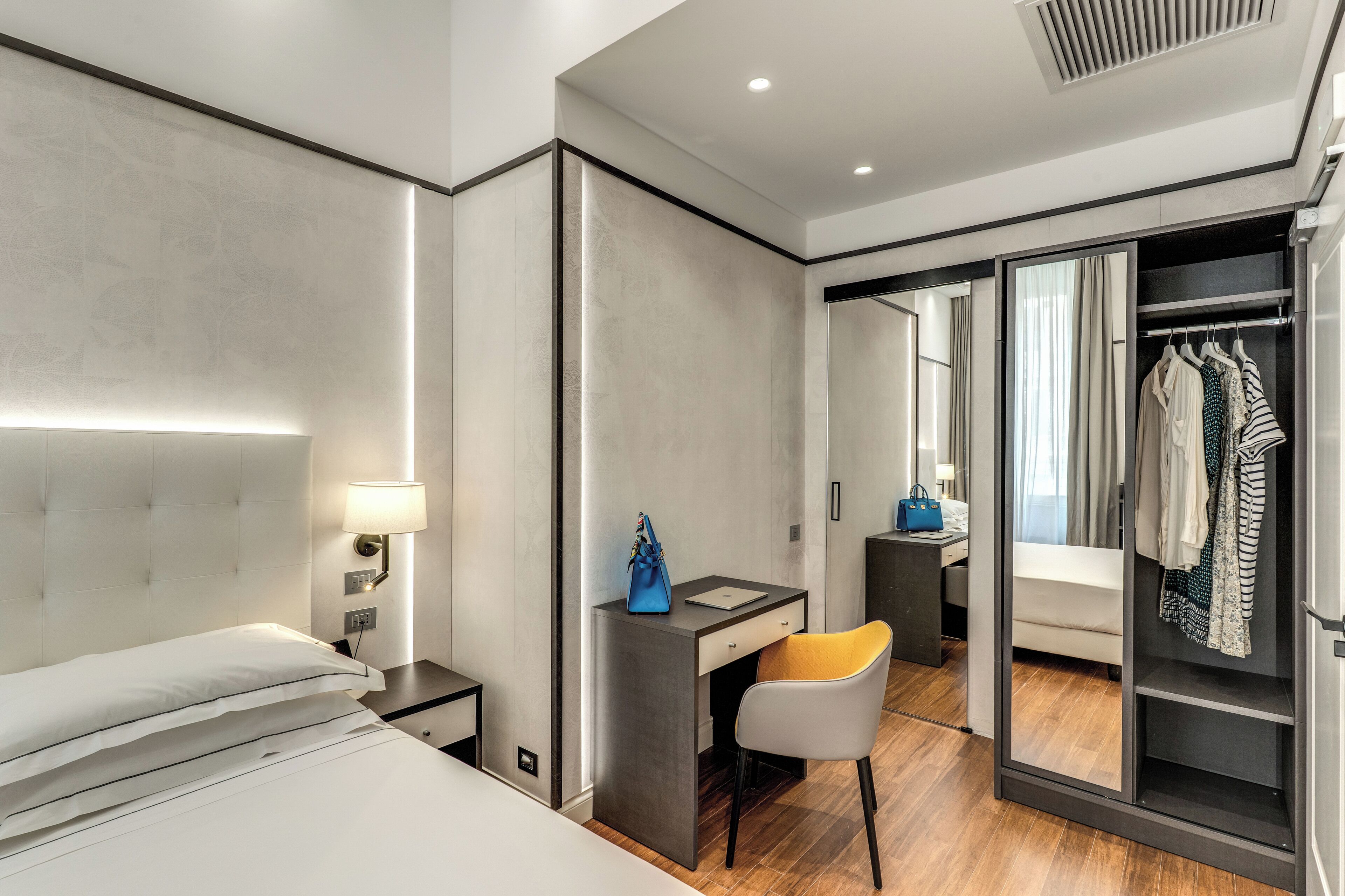 Una habitación de hotel moderna con cama, escritorio, silla, armario y espejo.