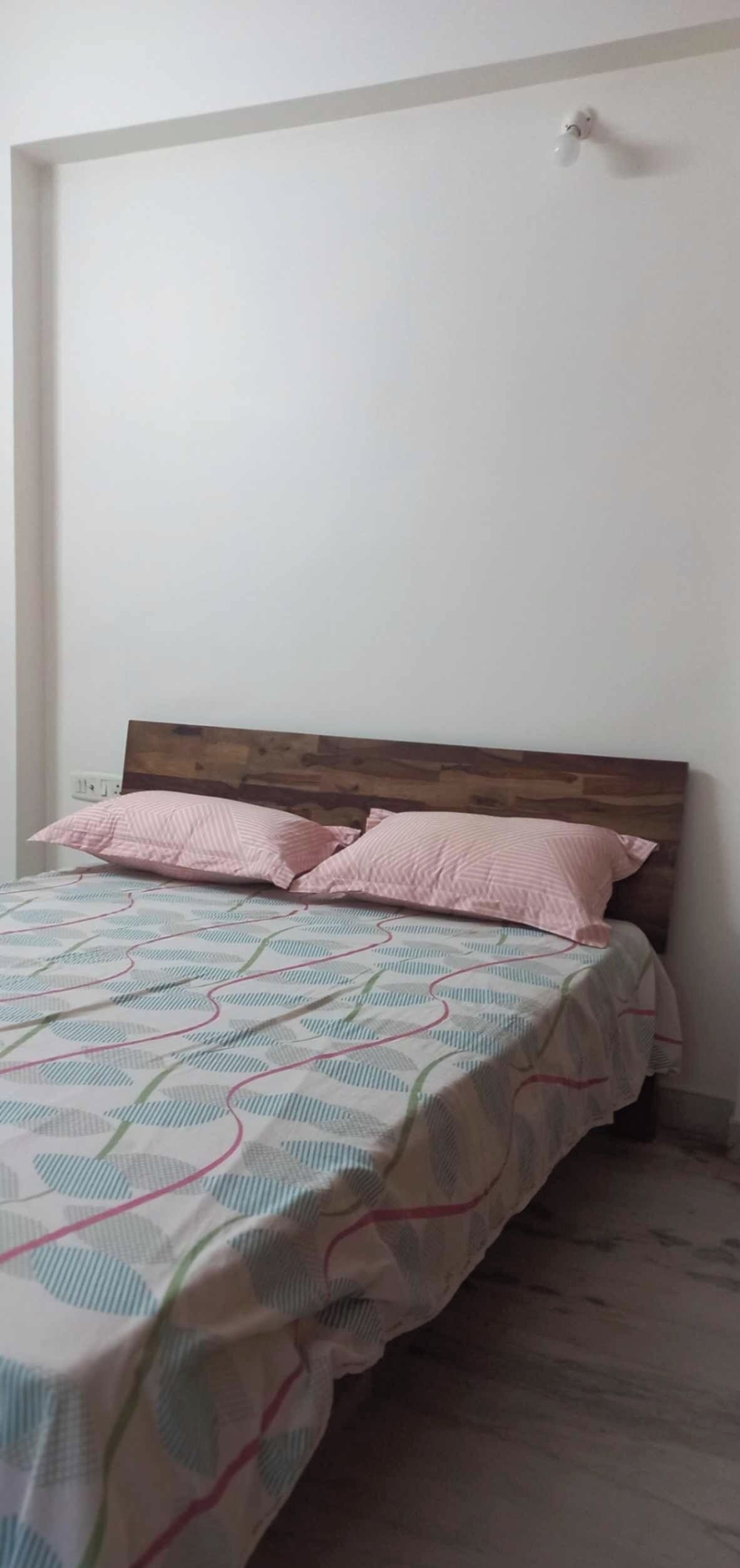 A bedroom with a wooden headboard, a bed with a patterned bedspread, and two pink pillows.