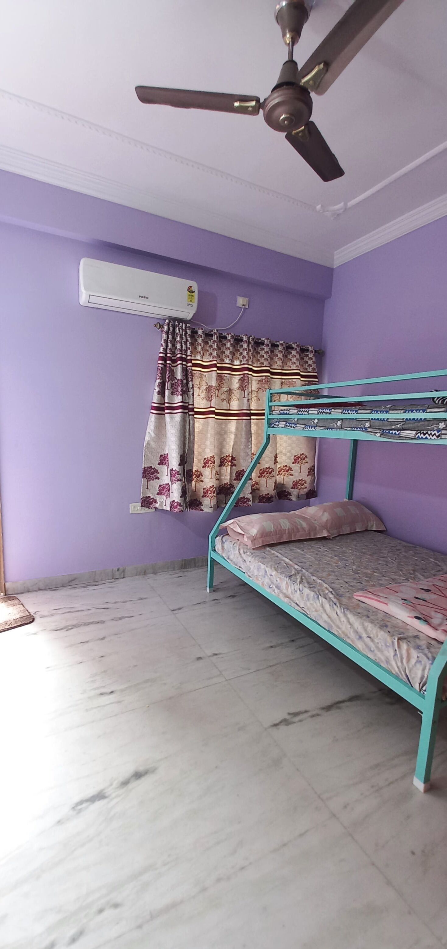 A room with a bunk bed, an air conditioning unit, a ceiling fan, and a window with patterned curtains.