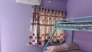 A room with a bunk bed, an air conditioning unit, a ceiling fan, and a window with patterned curtains.