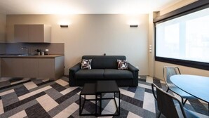 Un espacio habitable compacto con kitchenette, un sofá con cojines estampados, una mesita y una zona de comedor.