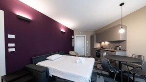 Una habitación de hotel compacta con una cama, mesitas de noche, un escritorio y una kitchenette.