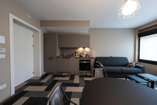 A compact living space with a kitchenette, a sofa, a dining table, and a view through a window.