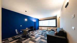 Una habitación moderna con una pared azul de acento, un sofá, una mesa de comedor con sillas y un ventanal que proporciona luz natural.