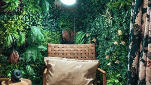 Une pièce comprenant une chaise en bois, une petite table, une lampe et un mur recouvert de plantes artificielles.