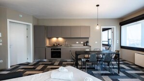 A modern hotel room with a bed, a dining area, and a kitchenette.