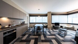 A modern kitchen with a dining area, large windows, and a flat-screen TV.