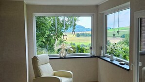 Una habitación con un sillón color beige junto a un ventanal grande con vistas a un paisaje verde.