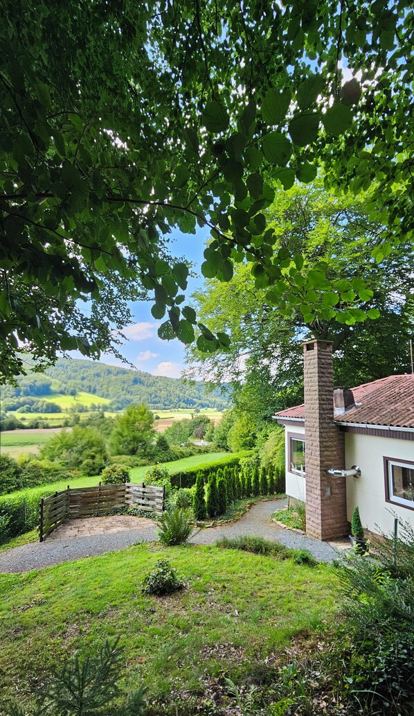 A house with a brick chimney, surrounded by a well-maintained garden and a view of rolling hills.