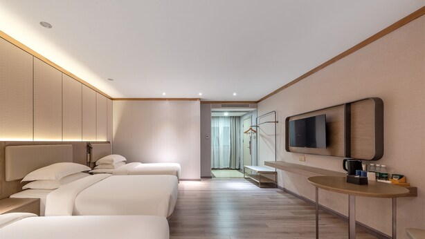 A hotel room with a large bed, a bedside table, a TV mounted on the wall, and a small table with a coffee maker. - KAJI Hotel (Guangzhou)