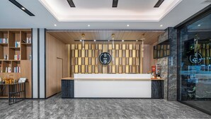 A modern reception area with a wooden panel wall, a reception desk, and a bookshelf with books. - KAJI Hotel (Guangzhou)