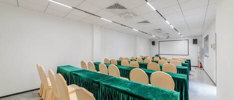A conference room with rows of tables and chairs, a projector screen, and a whiteboard.