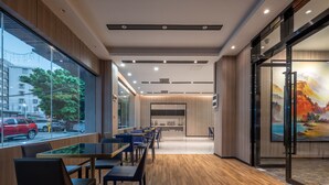 A modern restaurant with wooden flooring, glass tables, and chairs. It features a view of the street through large windows and a painting on the right wall. - KAJI Hotel (Guangzhou)