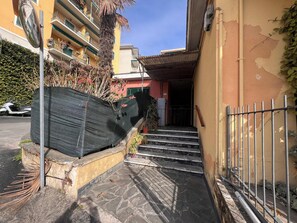 Un edificio residencial con una escalera que lleva a una puerta, una cerca de metal y un scooter estacionado.
