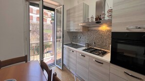 Une cuisine moderne équipée d’une cuisinière à gaz, d’un évier et de placards. On y trouve une table à manger avec des chaises, ainsi qu’une porte-fenêtre coulissante donnant sur un balcon.
