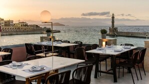 Un espacio de comedor al aire libre con mesas y sillas, con vistas a un cuerpo de agua y una isla distante.