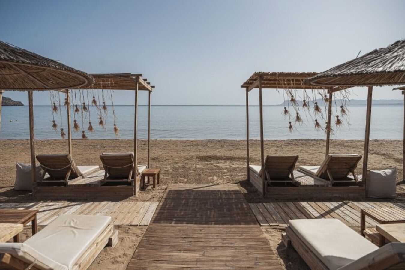 A beach with wooden cabanas, lounge chairs, and a wooden deck.