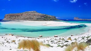 Un paisaje costero con una colina rocosa destacada, aguas turquesas cristalinas y una playa de arena.