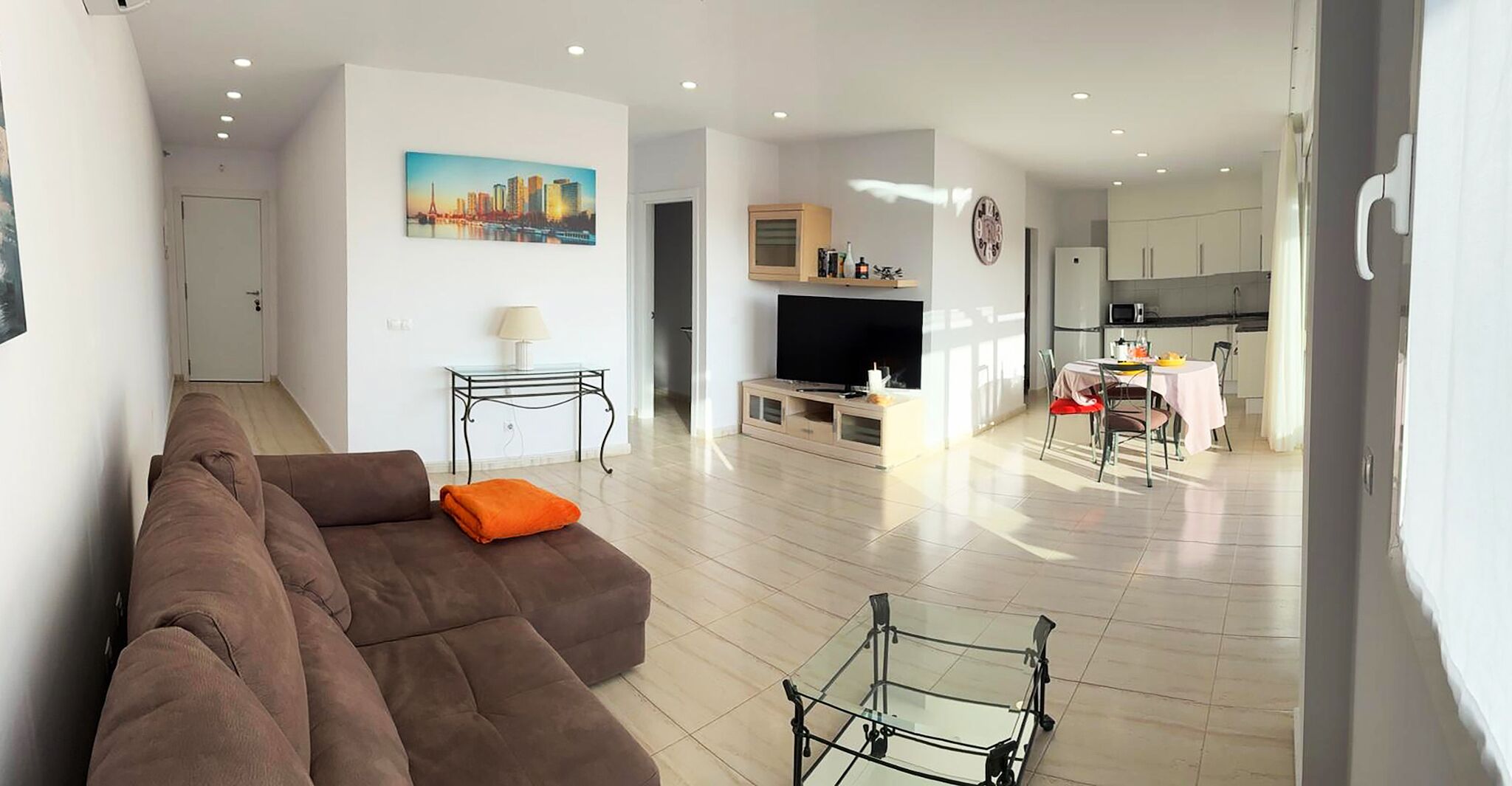 A modern living room with a brown sofa, a glass coffee table, and a painting of a cityscape.