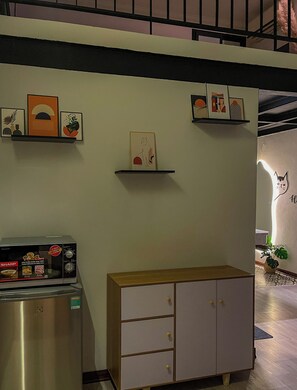Una cocina con refrigerador, microondas y un armario. Hay repisas en la pared con objetos decorativos.