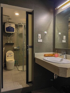 Un baño moderno con cabina de ducha de vidrio, un inodoro con un adhesivo que dice 'Adiós' y un lavabo con dispensador de jabón.