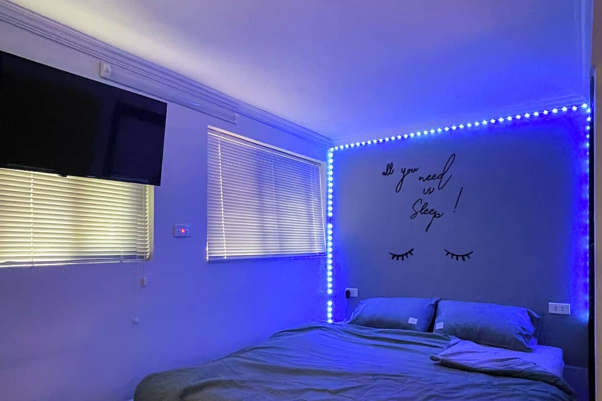 A bedroom with a bed, a wall-mounted TV, and a sign that says "You need sleep!" with eye illustrations.