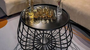 Een moderne woonkamer met een bank, een ronde salontafel met decoratieve objecten, een lamp en een wand met een structuur.